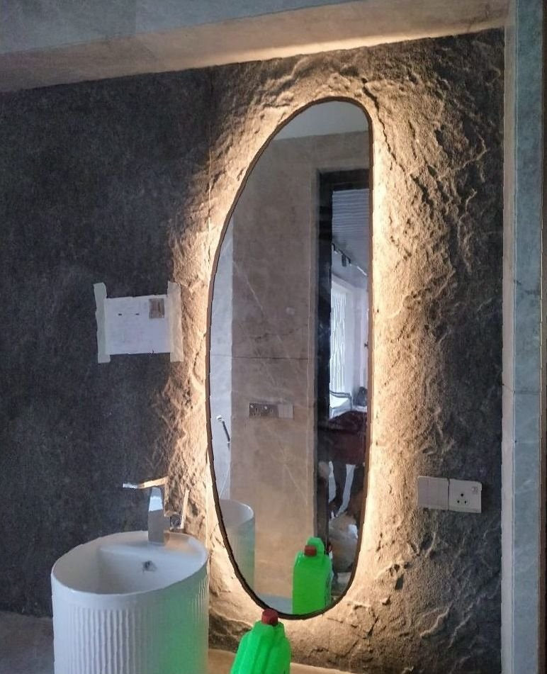 Backlit metal-framed oval mirror on a textured stone wall