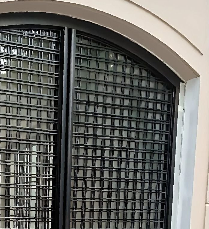 Blackened steel screen over an arched facade window