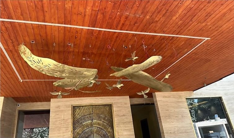 Brass bird installation suspended below a timber ceiling