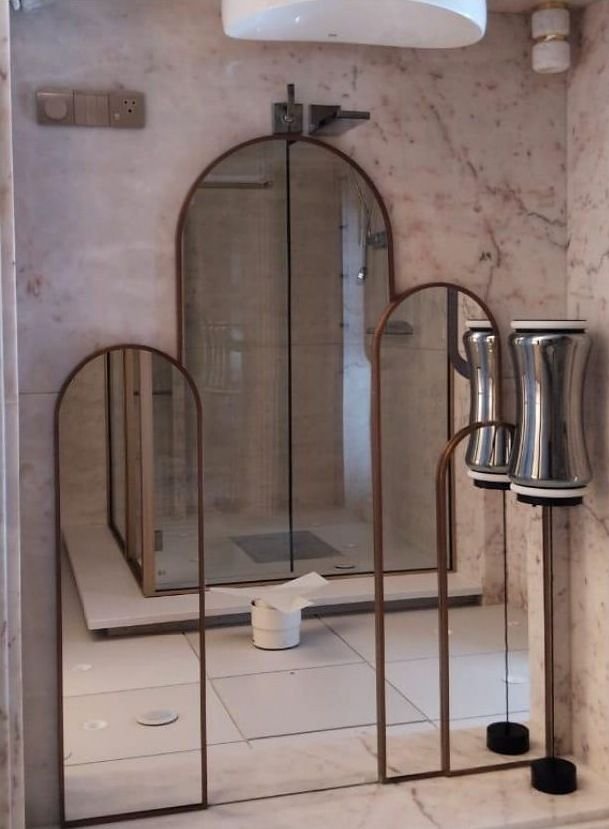 Brass-framed arched mirror panels in a marble bathroom