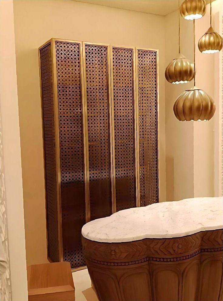 Brass mesh folding screen beside a carved bathtub in a hotel suite