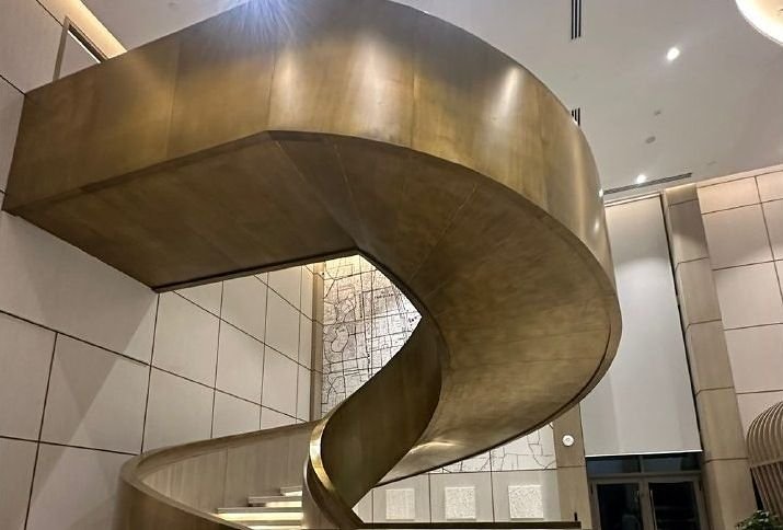 Bronze-finished spiral staircase curving through a marble-clad lobby