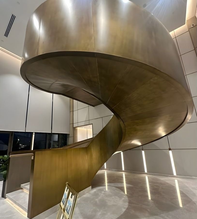 Underside of a sculpted bronze spiral staircase showing its continuous folded soffit