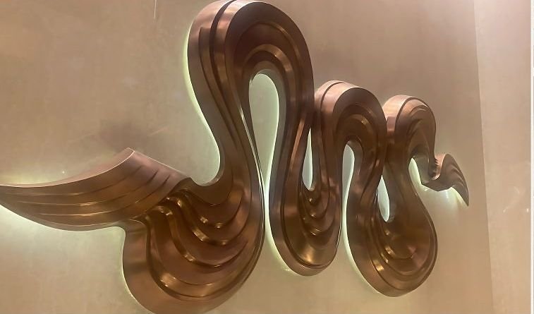 Polished copper wave sculpture mounted on a wall