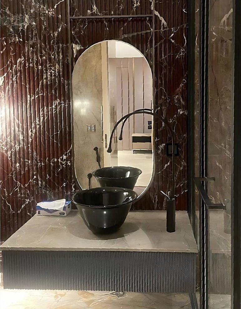Metal-framed mirror above a stone vanity in a marble bathroom