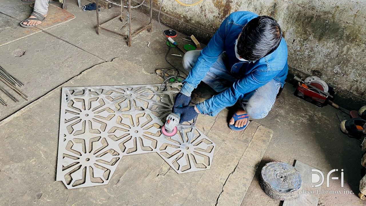 Craftsman hand-finishing a cut metal jaali panel on the workshop floor