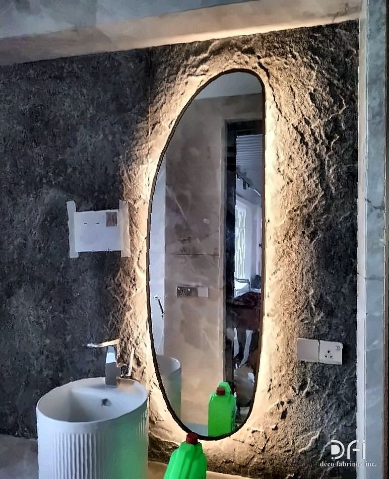 Backlit metal-framed oval mirror on a textured stone wall