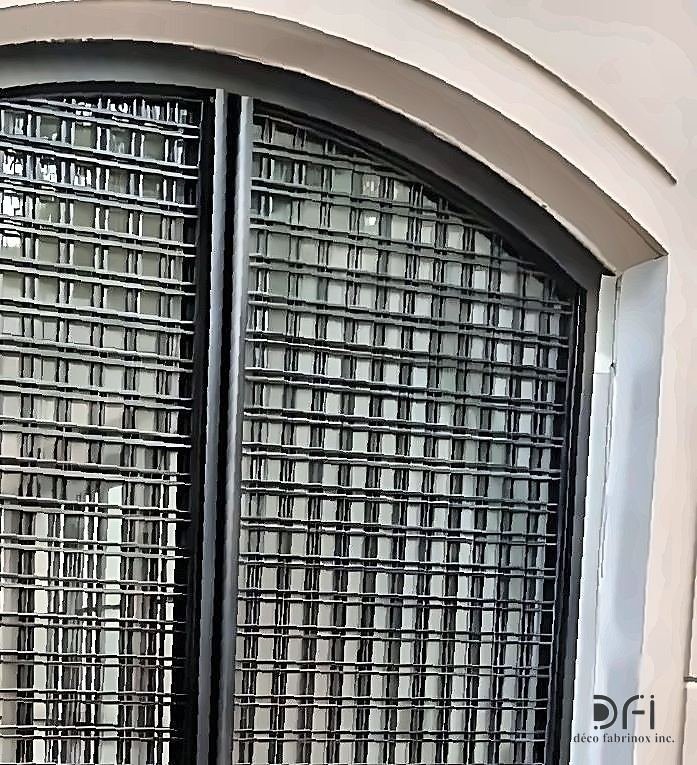 Blackened steel screen over an arched facade window
