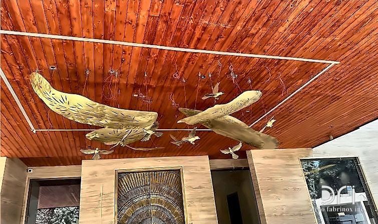 Brass bird installation suspended below a timber ceiling