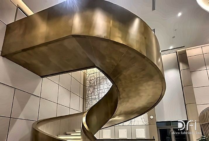 Bronze-finished spiral staircase curving through a marble-clad lobby