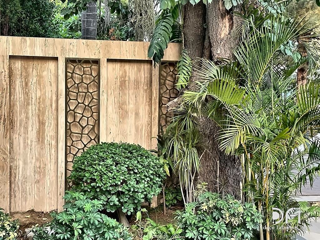 Stone garden wall with a laser-cut metal jaali panel, by day