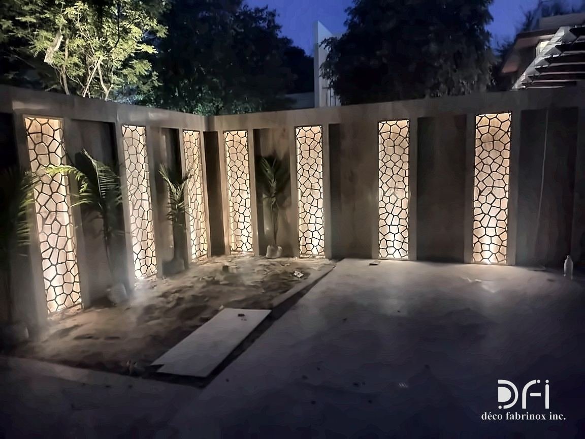 Boundary wall with laser-cut metal panels lit from behind at night