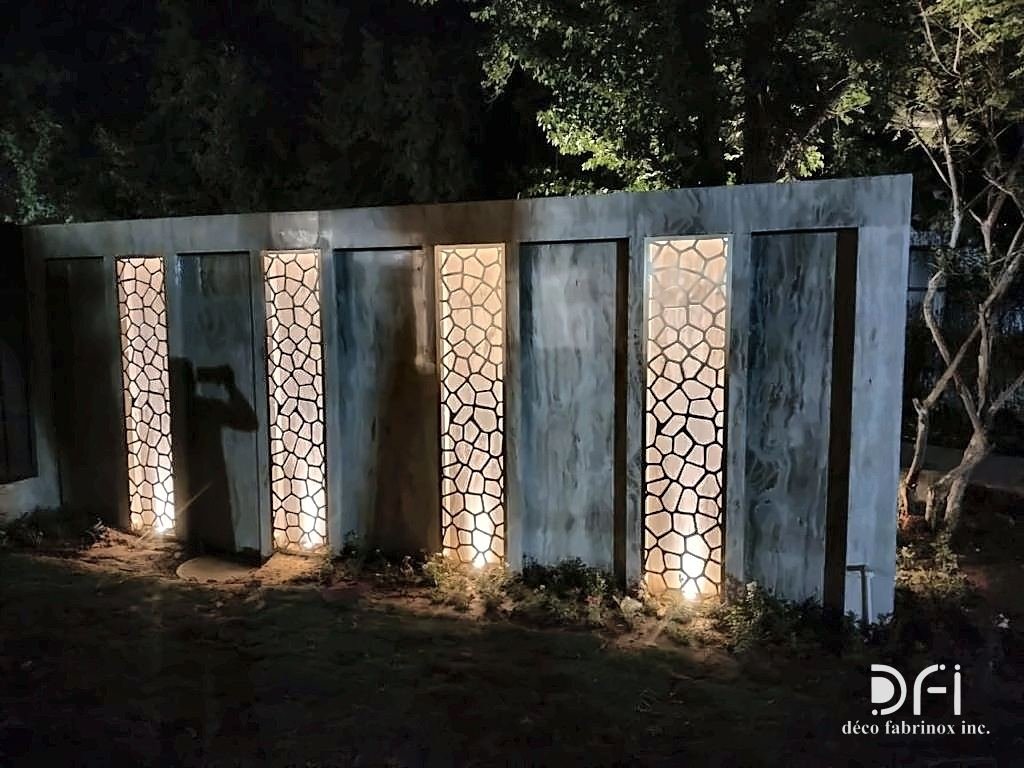 Laser-cut metal jaali panels set into a stone garden wall, lit at night