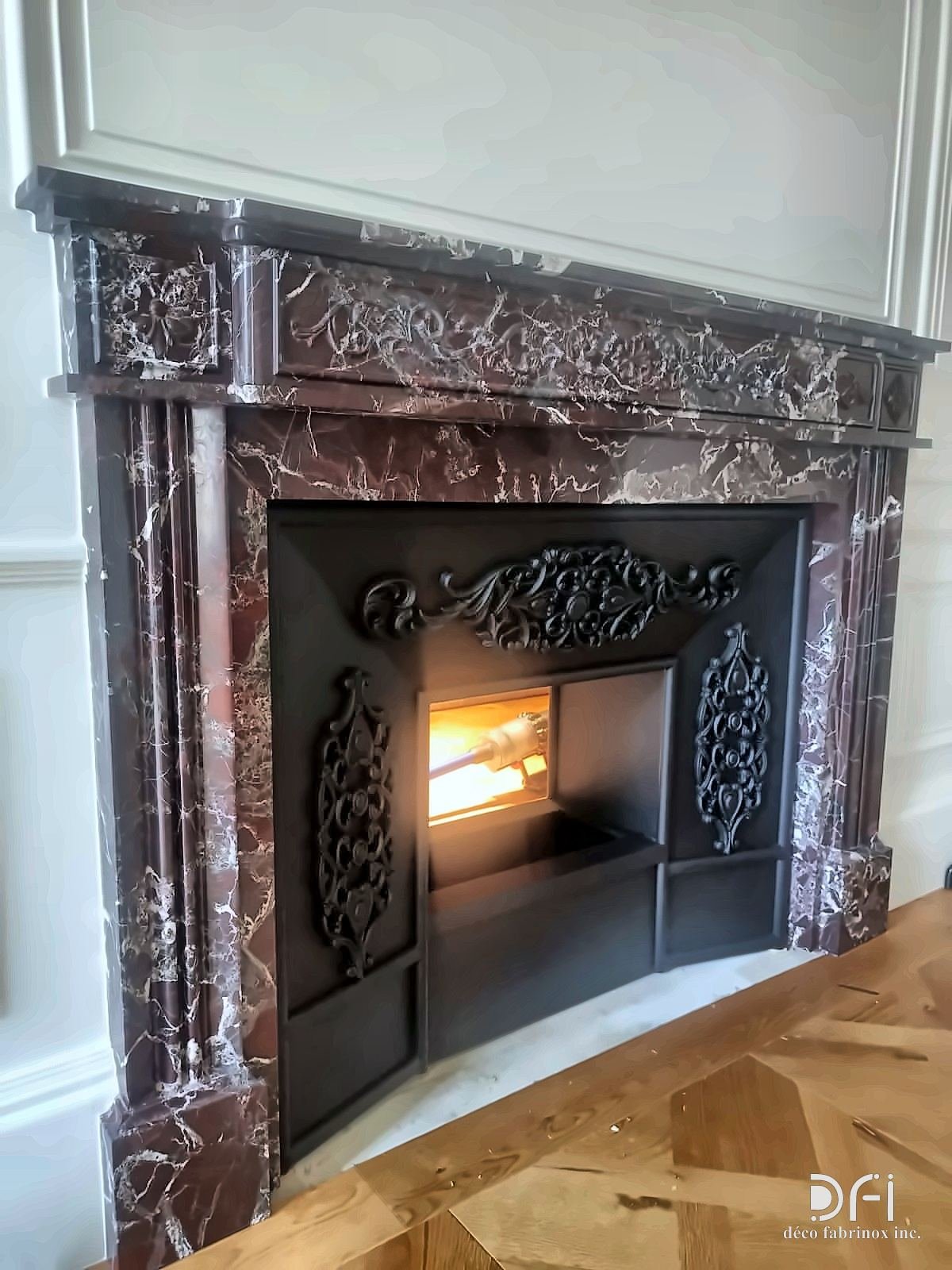 Red marble fireplace with a black ornamental metal front, fire lit