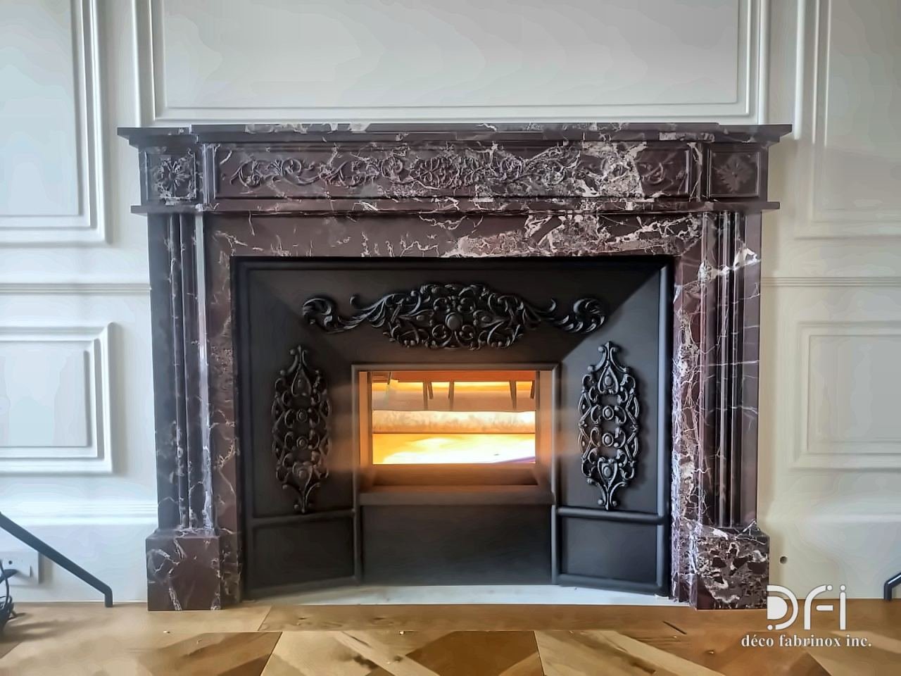 Marble fireplace surround with a lit fire behind an ornamental black metal front