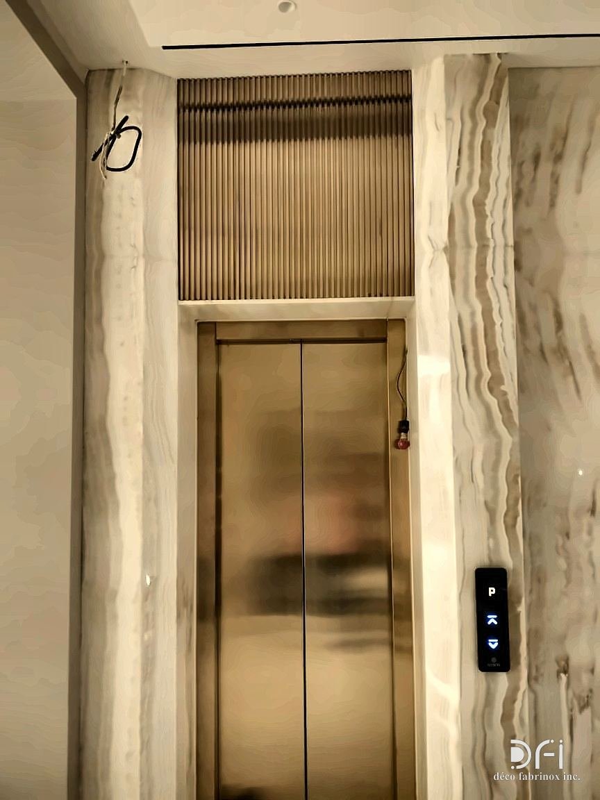 Gold-toned metal lift doors and transom set between marble walls