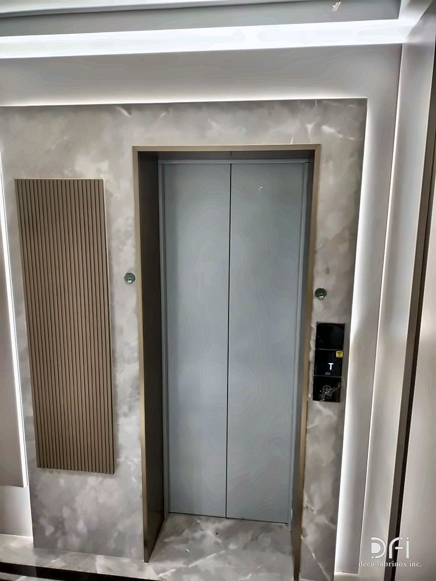 Lift entrance with a slim stainless frame and a fluted metal side panel