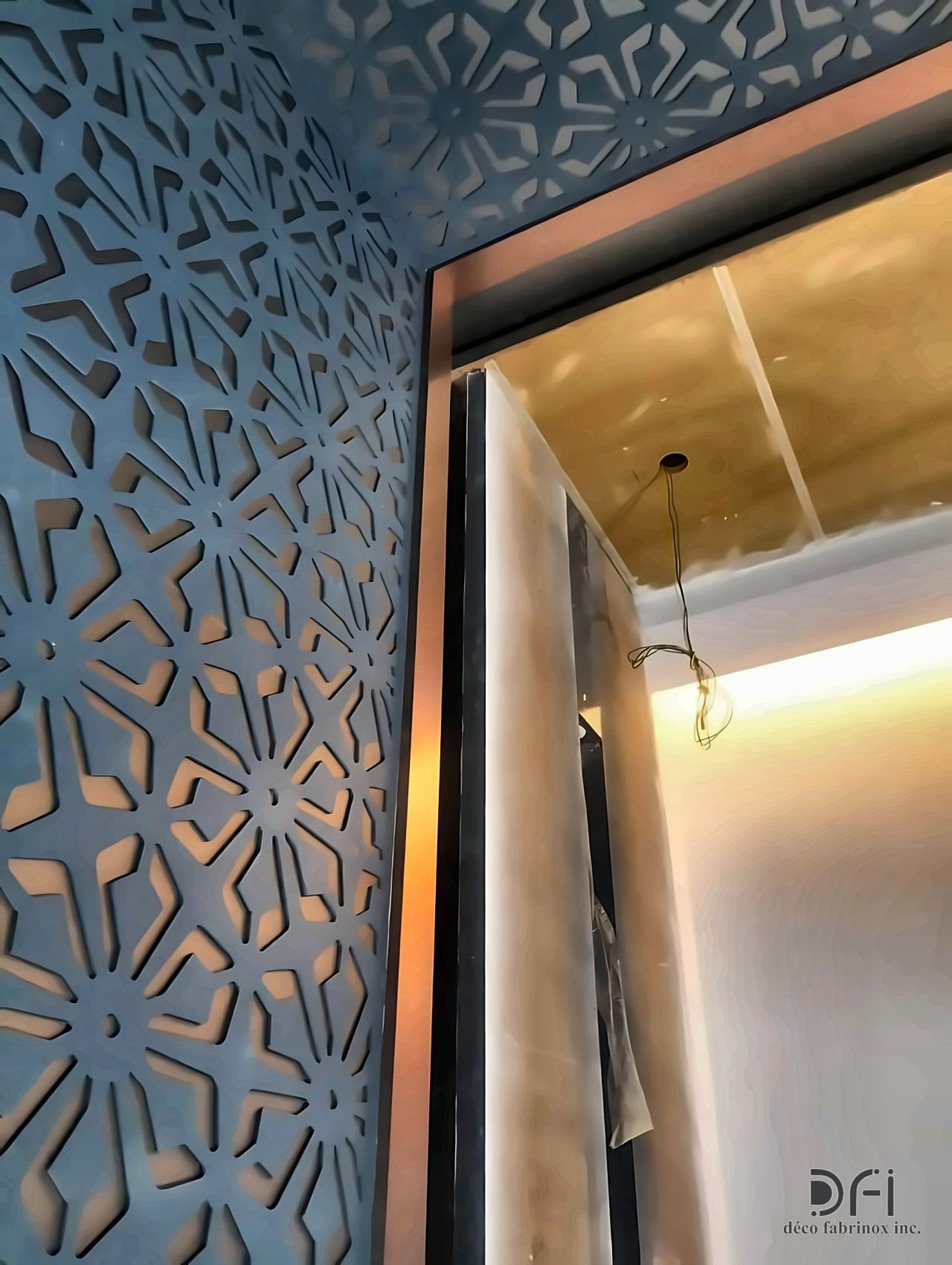 Laser-cut geometric metal wall beside a brass-clad doorway