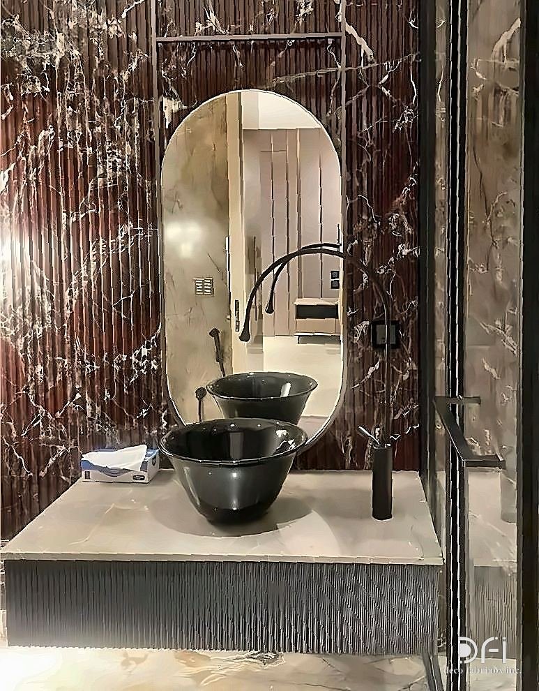 Metal-framed mirror above a stone vanity in a marble bathroom