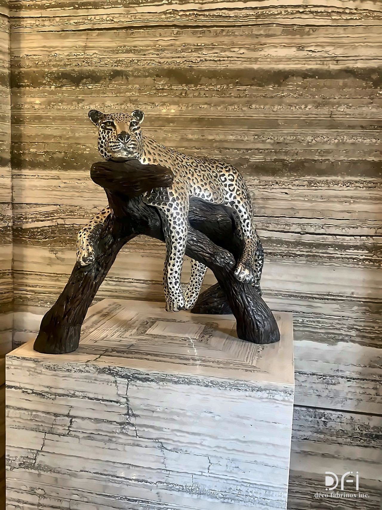 Bronze leopard sculpture on a branch, on a stone plinth