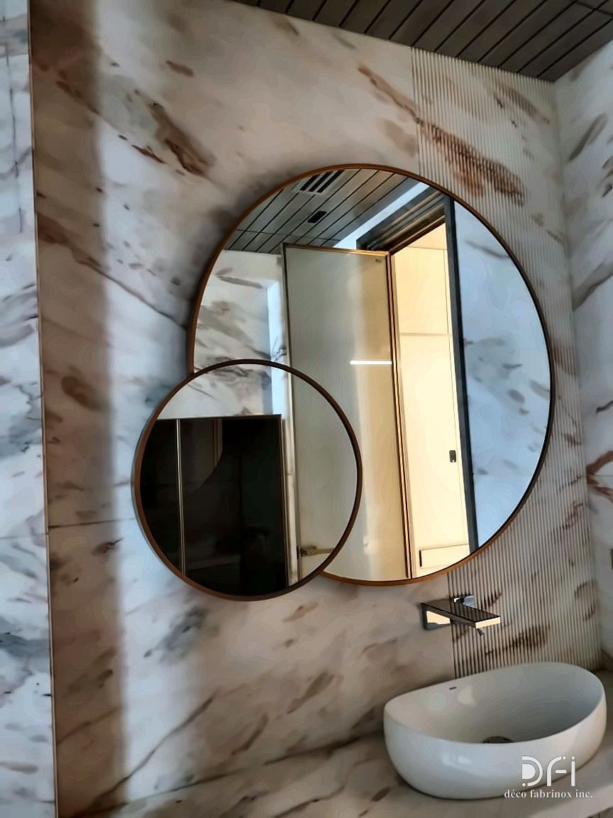 A large and a small round metal-framed mirror overlapping on a marble wall