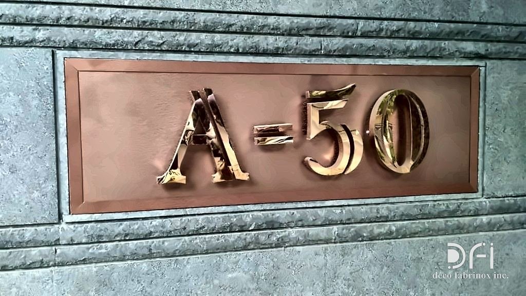 Copper house-number plaque with raised letters, set into a stone wall