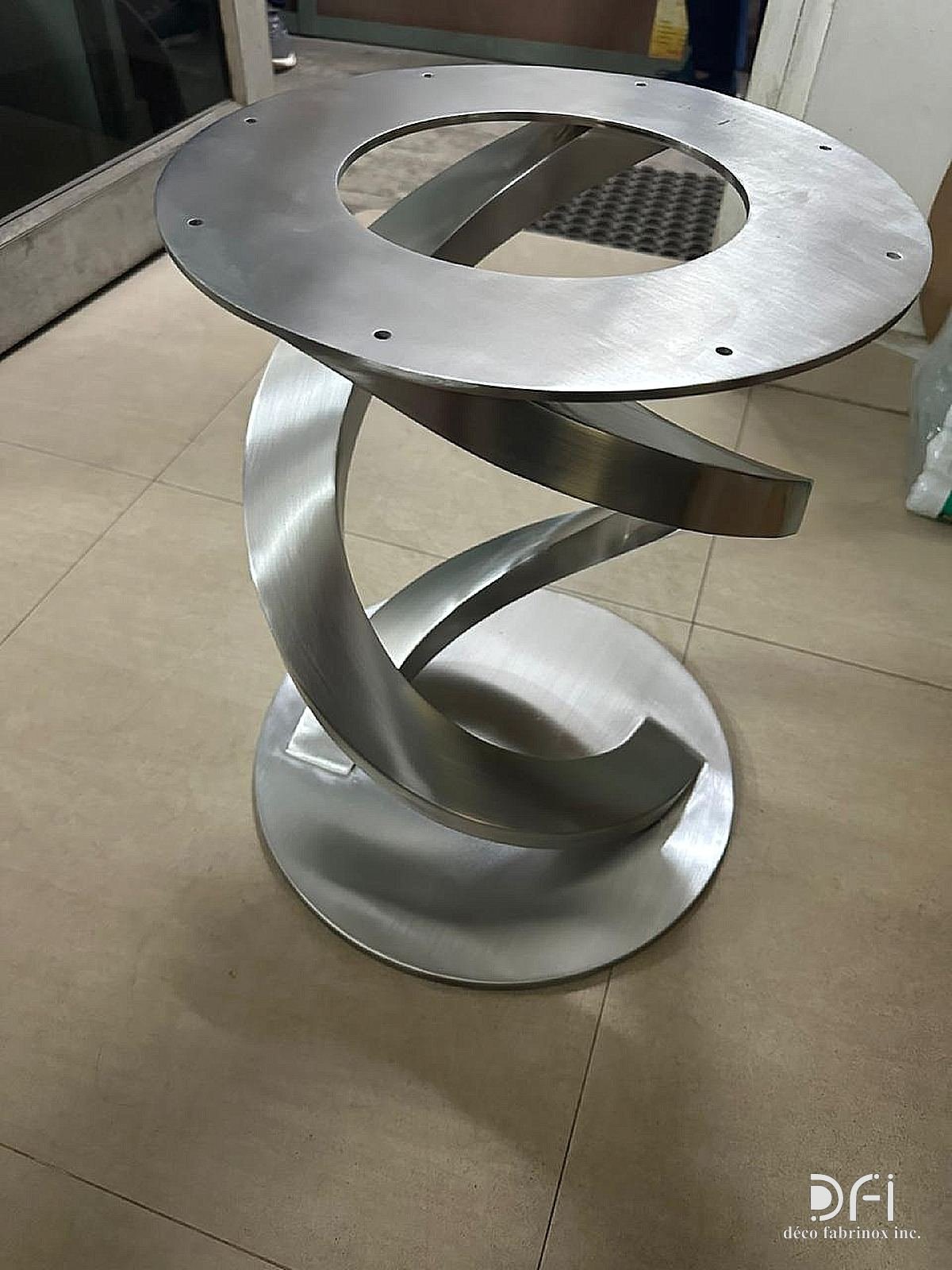Sculptural twisted brushed-steel table base with a ring top frame